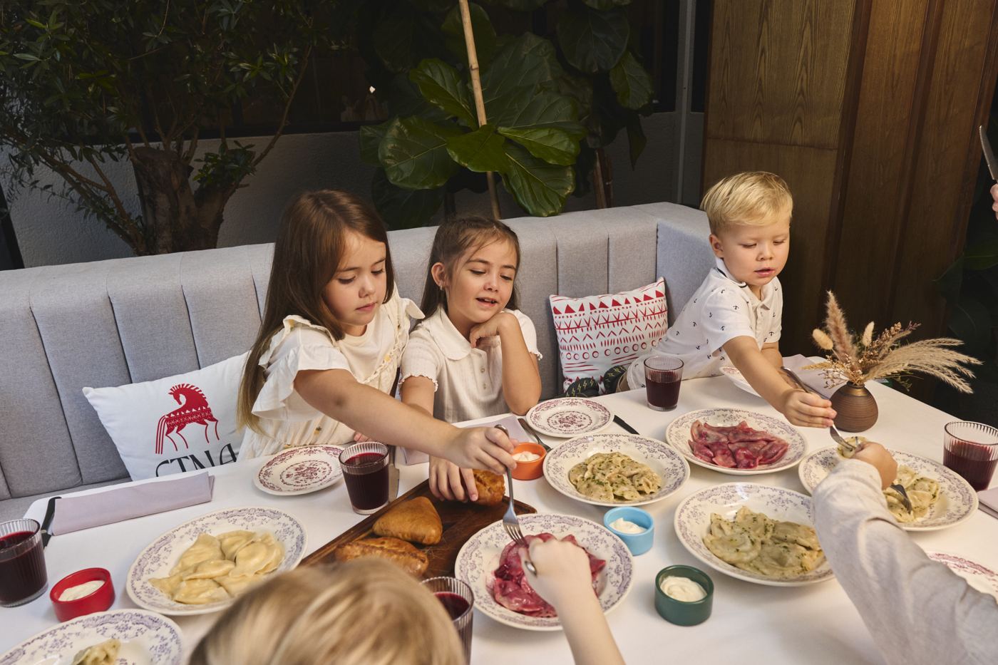 Three kids at the ETNA table with pelmeni and the red-horse pillow