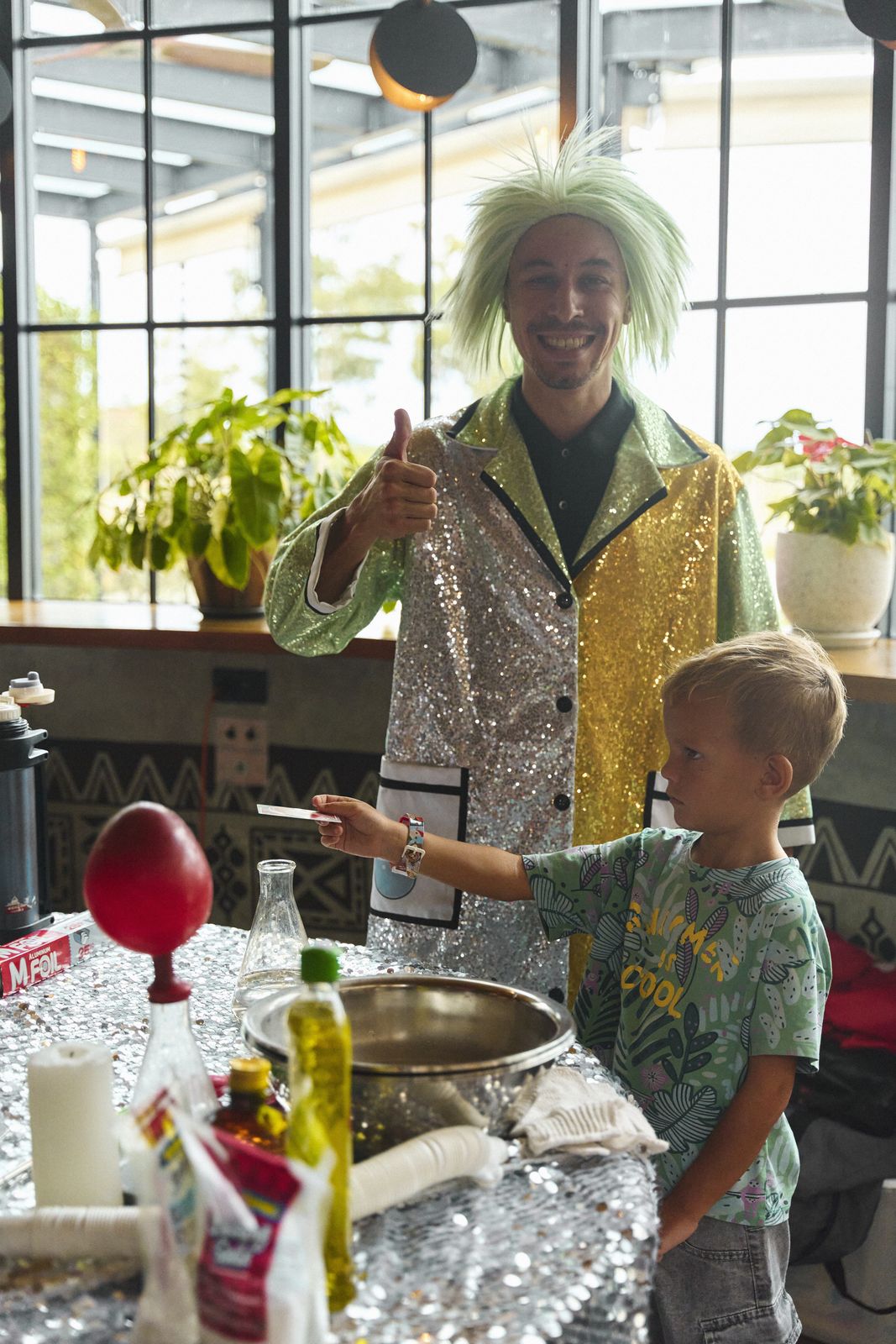 Science show host with green hair and kids at the ETNA table